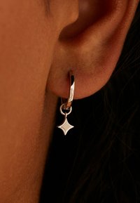 Zilveren creool met een kleine, diamantvormige hanger. Het ontwerp is glad en gepolijst, met een strak, reflecterend oppervlak.