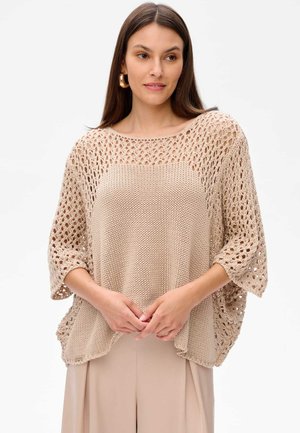 Top en tricot beige avec des accents en crochet ajouré, des manches larges et une coupe décontractée. Présente un col rond et un tissu texturé.