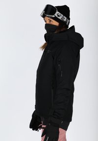 Black insulated ski jacket with a hood, zippered pockets, paired with a black beanie and ski goggles. Gloves complete the winter sports attire.