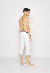 Hvide capri leggings med en sort elastisk talje med logo detalje, glat tekstur og tætsiddende design, vist fra en sidevinkel.