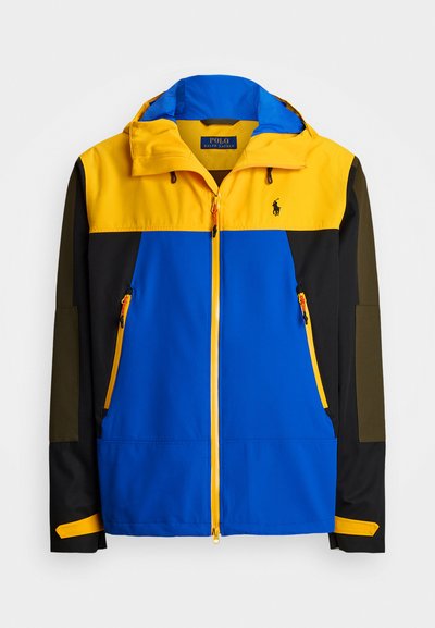 Spalvota striukė su geltonu kapišonu ir viršutine dalimi, mėlyna kūno dalimi, juodomis rankovėmis ir oranžinėmis užtrauktuko detalėmis. Pagaminta iš lengvos medžiagos.