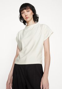 Top corto a maniche corte, di un delicato color crema, con scollatura rotonda e una texture morbida, abbinato a pantaloni neri a vita alta. Design moderno e minimale.