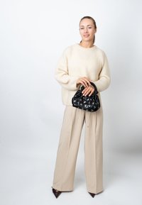 Kremasti pleteni džemper, bež široke hlače i crna torba sa naborima i metalik detaljima. Izgled upotpunjuju smeđe šiljaste potpetice.