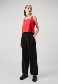 Red cropped tank top with square neckline, paired with high-waisted black wide-leg trousers and chunky black shoes with studded accents.