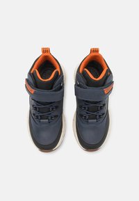 Baskets synthétiques navy et noir avec intérieur orange, comprenant des lacets et une sangle ajustable, bout arrondi et semelle en caoutchouc texturée.