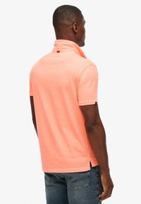 Poloshirt met korte mouwen in levendig koraal, gemaakt van zachte katoen. Voorzien van een kraag en zijsplitten. Op de achterkant bevindt zich een klein merkembleem vlak bij de halslijn.