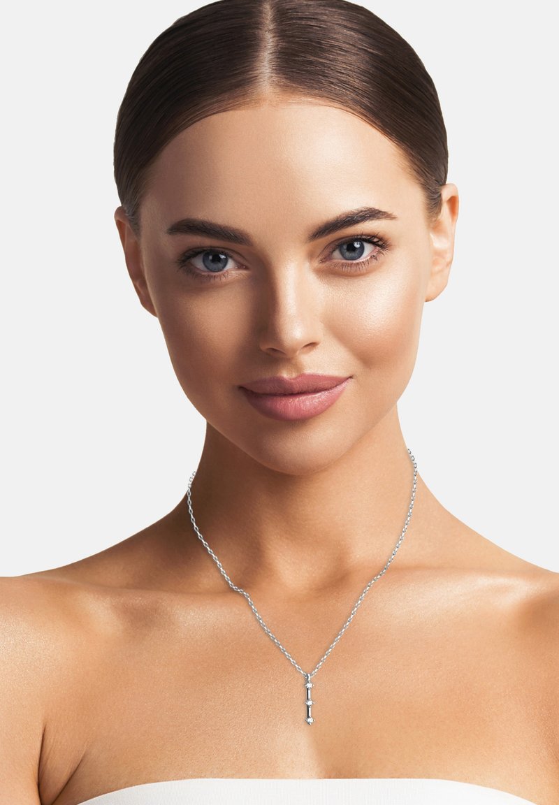 Silversmycke med hängande design som har geometriska former, vilande på en tunn kedja mot bar hud.