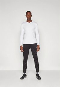 Biela tričko s dlhými rukávmi a výstrihom do V, spárované s čiernymi športovými nohavicami s logom, navrhnuté pre aktívne nosenie, s priliehavým strihom a hladkou textúrou.