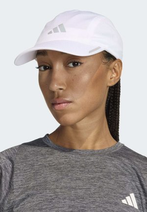 Gorra blanca con un acabado texturizado, que presenta acentos grises y un logo de tres franjas. El modelo lleva una camiseta atlética gris.