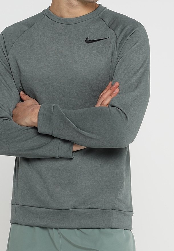 Szara bluza Nike z długim rękawem, okrągłym dekoltem i prążkowanymi mankietami. Posiada czarne logo na górnej lewej części klatki piersiowej. Miękka w dotyku.
