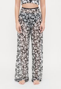Pantaloni a gamba larga con stampa floreale, realizzati in tessuto leggero e trasparente, con uno sfondo nero e fiori bianchi e grigi. Visibile la cintura elastica.