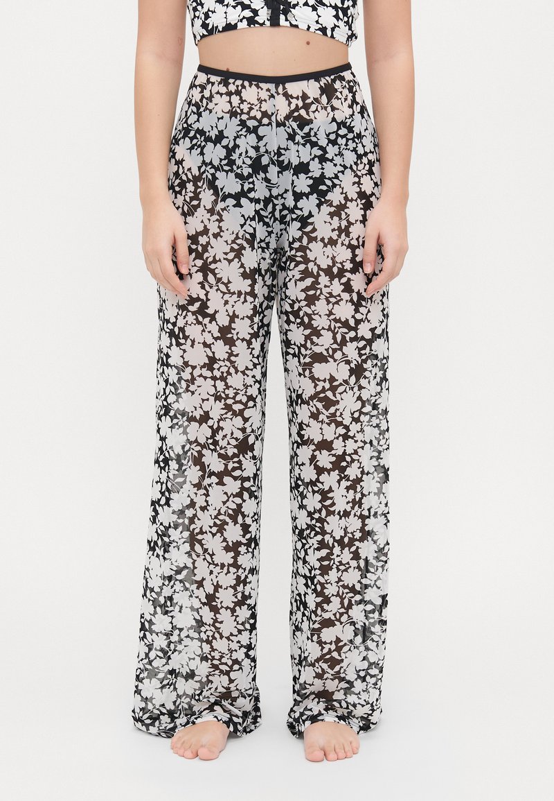 Pantaloni a gamba larga con stampa floreale, realizzati in tessuto leggero e trasparente, con uno sfondo nero e fiori bianchi e grigi. Visibile la cintura elastica.