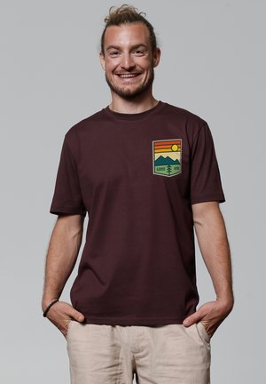 Bordeaux katoenen T-shirt met een graphic van bergen, de zon en de tekst "Good Vibe." Korte mouwen en ronde hals.