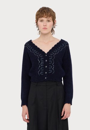 Marinblå stickad cardigan med vågig halsringning, dekorerad med blåa pärlor och knappstängningar, med långa ärmar och kort design.