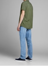 Olijfgroen shirt met korte mouwen en een ontspannen pasvorm, gecombineerd met lichtblauwe straight-leg jeans en marineblauwe sneakers met witte accenten.