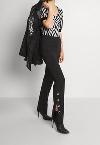 Top de punto a rayas en blanco y negro con escote en V y mangas cortas, combinado con pantalones negros que presentan detalles de botones plateados y aberturas.