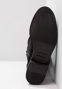 Botte en daim noir avec une semelle en caoutchouc texturée, dotée d'un talon, taille 37, avec des détails en relief sur la semelle pour l'adhérence.