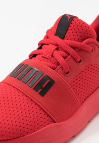Chaussure de sport rouge en matériau mesh, avec une semelle intermédiaire épaisse et une bande noire bien visible affichant le logo "PUMA" sur le devant.