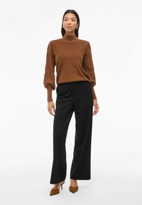 Pull en maille marron à col haut avec des manches bouffantes, assorti à un pantalon large noir et des escarpins à bout pointu marron. Textures simples et lisses.