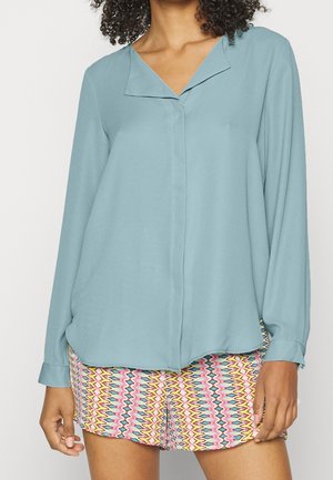Blusa azzurro chiaro con scollatura a V, maniche lunghe e vestibilità rilassata. Dettaglio notevole include pantaloni corti a fantasia con un design a zigzag colorato.