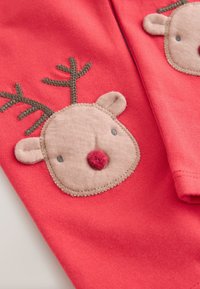 Tessuto di cotone rosso con applicazione di renna color fango con dettagli ricamati, tra cui corna, occhi e naso rosso. Texture morbida.