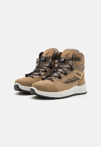 Stivali da trekking marroni con una tomaia in suede e sintetico, caratterizzati da accenti neri, un design con lacci e una suola bianca imbottita per la trazione.