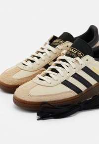 Beige su�ède en leren sneakers met zwarte strepen en veters, met een getextureerde neus en een bruine rubberen zool. Gouden branding op de tong.