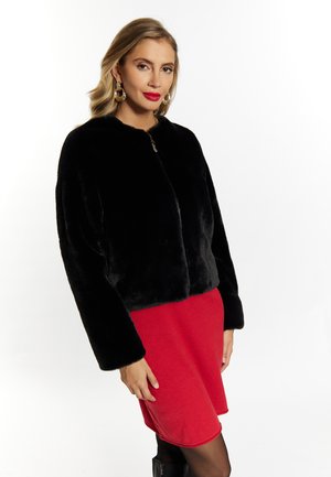 Schwarze Kunstpelzjacke mit rundem Ausschnitt und Reißverschluss, getragen über einem roten Rock. Die Jacke hat lange Ärmel und ein kurzes Design.