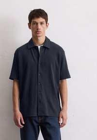 Marineblauw kortemouwen overhemd met knoopsluiting, gemaakt van een gestructureerde stof met verticale strepen, voorzien van een klassieke kraag en knopen aan de voorkant.