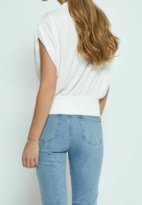 Top blanco de manga corta con un respaldo fruncido, combinado con jeans ajustados de color azul claro. Tela suave con un ajuste relajado y detalles en la cinturilla.