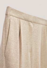 Beżowe spodnie z zakładkami wykonane z teksturowanej tkaniny z wzorem w jodełkę, z usztywnionym pasem i gładkim wykończeniem.