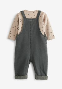 Chemise beige à manches longues avec des pois abstraits noirs sous une salopette en denim gris foncé avec des poignets retroussés, vue de dos sur fond blanc.
