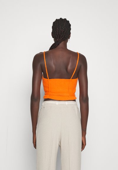 Πορτοκαλί ριγωτό crop top με λεπτές τιράντες και εφαρμοστή σχεδίαση, συνδυασμένο με ανοιχτό μπεζ υφασμάτινο παντελόνι με ψηλή μέση. Απλό λευκό φόντο.