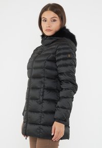 Cappotto imbottito nero con zip, dotato di cappuccio con bordo in pelliccia sintetica nera e design a pannelli cuciti.