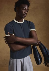 Tengerészkék rövid ujjú póló krémszínű bordázott gallérral és mandzsettával. A modellen mintás sál, világosszürke pliszírozott nadrággal párosítva.