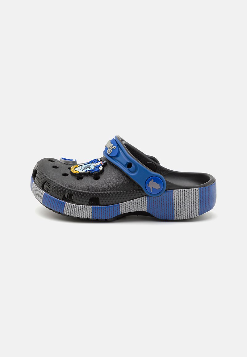 Black clogs with a blue strap, featuring ventilation holes, textured grey base, and decorative elements including colorful charms.