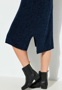 Zwarte leren enkellaarzen met een lage hak en gouden ritsdetails. Gecombineerd met een donkermariniënblaauw textuurjurk met een zijsplit.