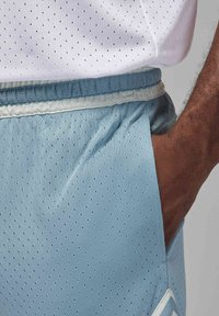 Šviesiai mėlyni sportiniai šortai su perforuota tekstūra, elastingu liemeniu ir šoninėmis kišenėmis. Matomos baltos ir šviesiai mėlynos juostelės akcentai.