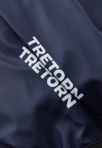 Tessuto blu navy con una superficie liscia, caratterizzato dal logo bianco "TRETORN" ben visibile. Il tessuto sembra leggero e flessibile.