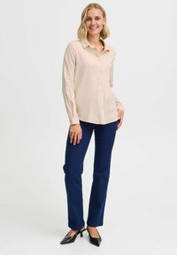 Camicia a maniche lunghe rosa chiaro con bottoni abbinata a pantaloni blu scuro a gamba dritta e tacchi neri a punta. Tessuto morbido e design sartoriale.