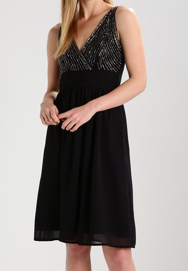 Svart klänning med V-ringning, utsmyckad med paljetter på bysten och en flödande kjol. Materialet verkar lätt och glatt, med en figurnära midja.