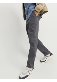 Graue Baumwollhose mit schlanker Passform, ausgestattet mit Seitentaschen und einer glatten Textur. Kombiniert mit weißen und blauen Sneakers.