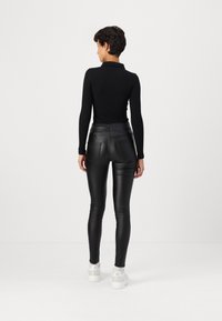 Zwarte langemouwen top gecombineerd met hoge taille zwarte faux leren broek. De outfit heeft een getailleerd ontwerp en een gladde textuur.