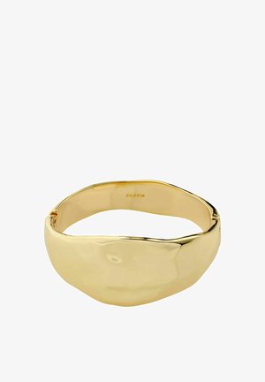 Złocona metalowa bransoletka z szeroką, nieregularnie ukształtowaną przednią płytką oraz gładką, wypolerowaną powierzchnią, z wytłoczonym napisem "PILGRIM" wewnątrz.