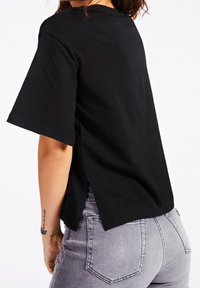 Camiseta negra de manga corta con cuello redondo, con aberturas laterales en el dobladillo, hecha de suave tejido de algodón. Combinada con jeans grises.
