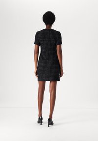 Svart tweedklänning med korta ärmar, figursydd design, texturerad tyg, knälång och en dold dragkedja bak. Bärs tillsammans med svarta klackar.