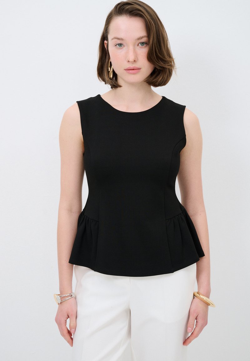 Schwarzes ärmelloses Peplum-Top mit rundem Ausschnitt, glatter Textur und dezenten Nähten, kombiniert mit hellfarbigen weit geschnittenen Hosen.