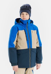 Kolorowa zimowa kurtka z niebieskim, beżowym i granatowym wzorem w blokach kolorów, z kapturem, zapinana na zamek z przodu i regulowanymi mankietami.