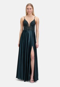 Robe longue vert émeraude avec un décolleté en V profond, un corsage orné, des bretelles fines et une fente sur le côté. Tissu en satin lisse avec une silhouette fluide.