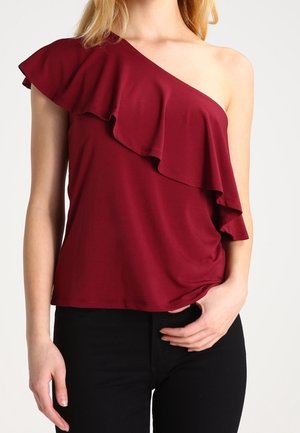 Burgunderfarbener One-Shoulder-Top mit gerafftem Design, aus weichem Stoff gefertigt, mit taillierter Silhouette und glatter Textur. Kombiniert mit schwarzen Hosen.